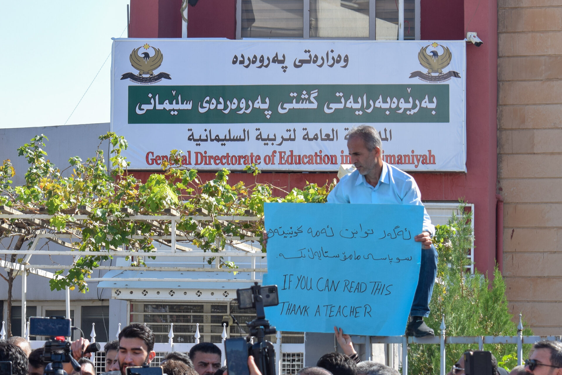 A teacher holds a sign in front of the General Directorate of Education during a protest by striking teachers in Sulaymaniyah on Oct. 22, 2023 (Winthrop Rodgers)