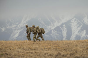 Three US Army servicemembers walking near mountains.
