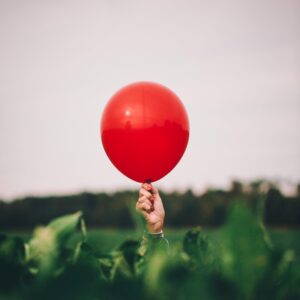 A person holds a red balloon in a field.