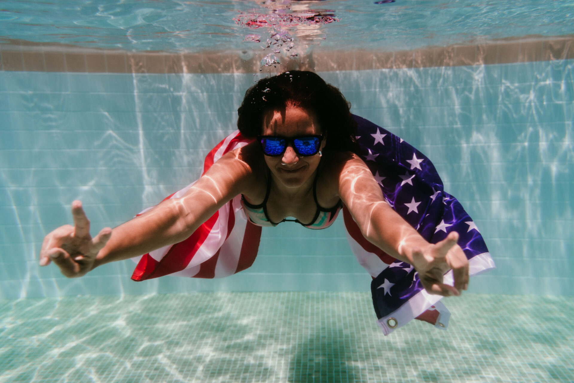 young woman in a pool holding american flag underwater. 4th july