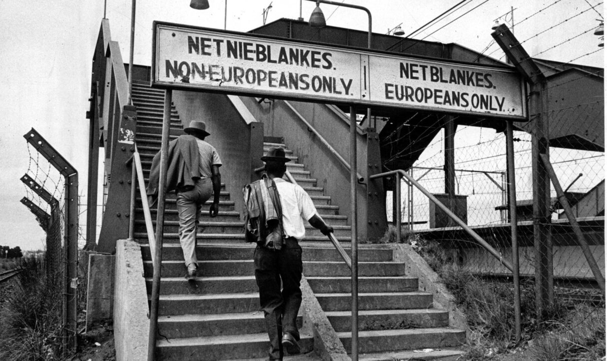 A sign during South Africa's apartheid era designates separate lanes for Black train passengers and white train passengers (Ernest Cole/Wikimedia Commons)