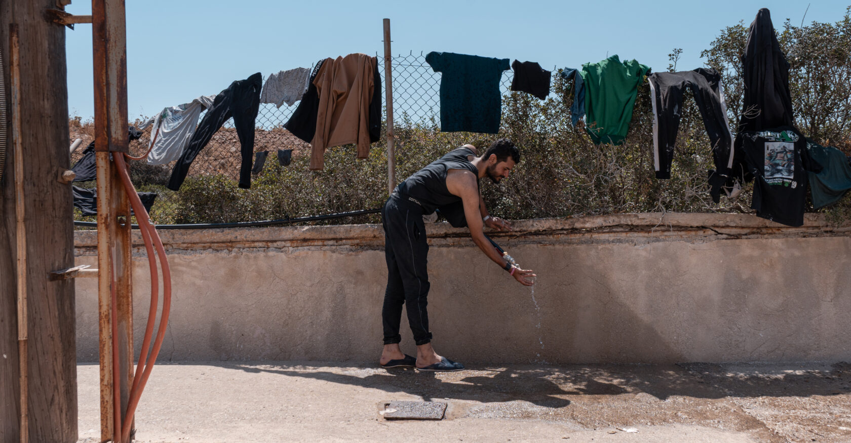 A man washes his clothing in a faucet outside a refugee facility in Crete (Sophia Potsi)