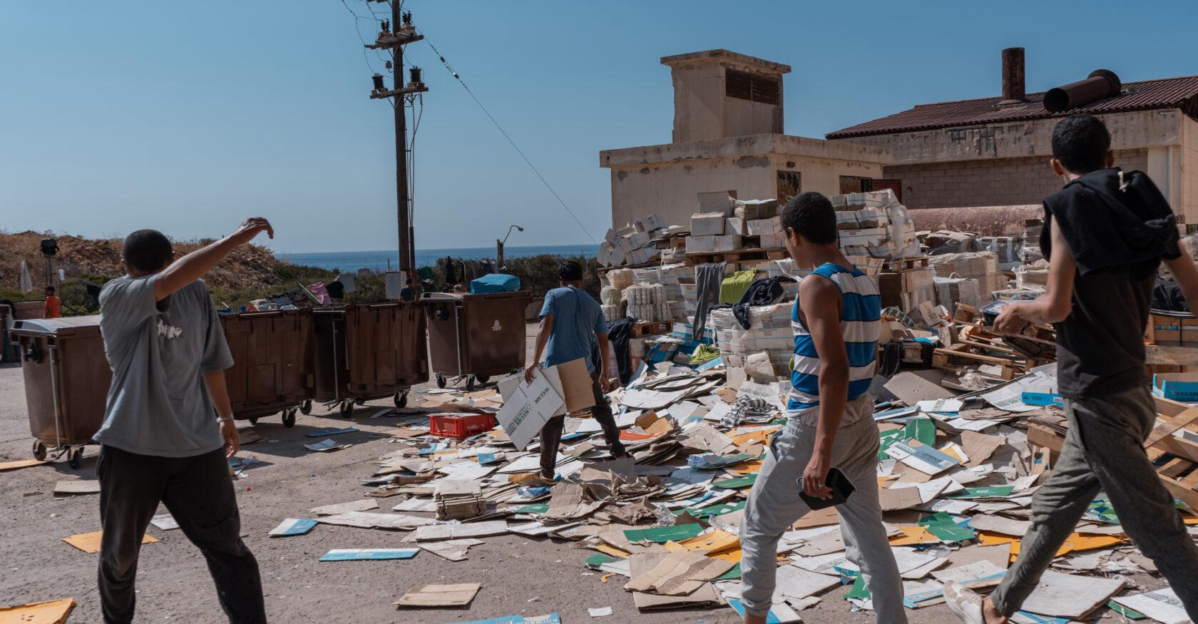 Men scavenge through a pile of discarded cardboard to build pallets for sleeping (Sophia Potsi)