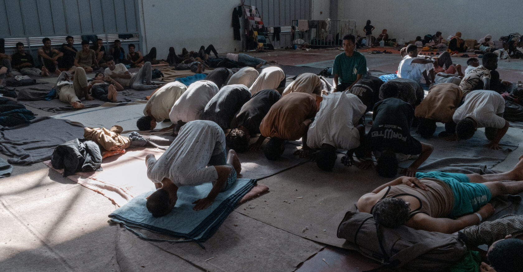 Men conduct prayers in the hall of a refugee facility (Sophia Potsi)