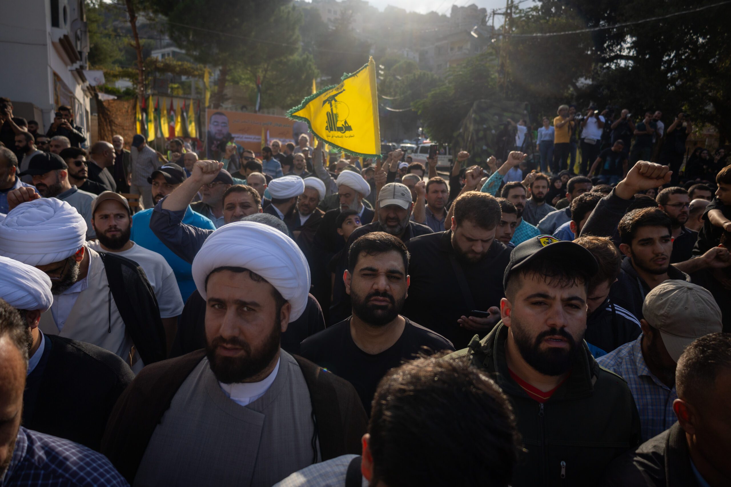 a crowd of people at a funeral in lebanon with a yellow flag.