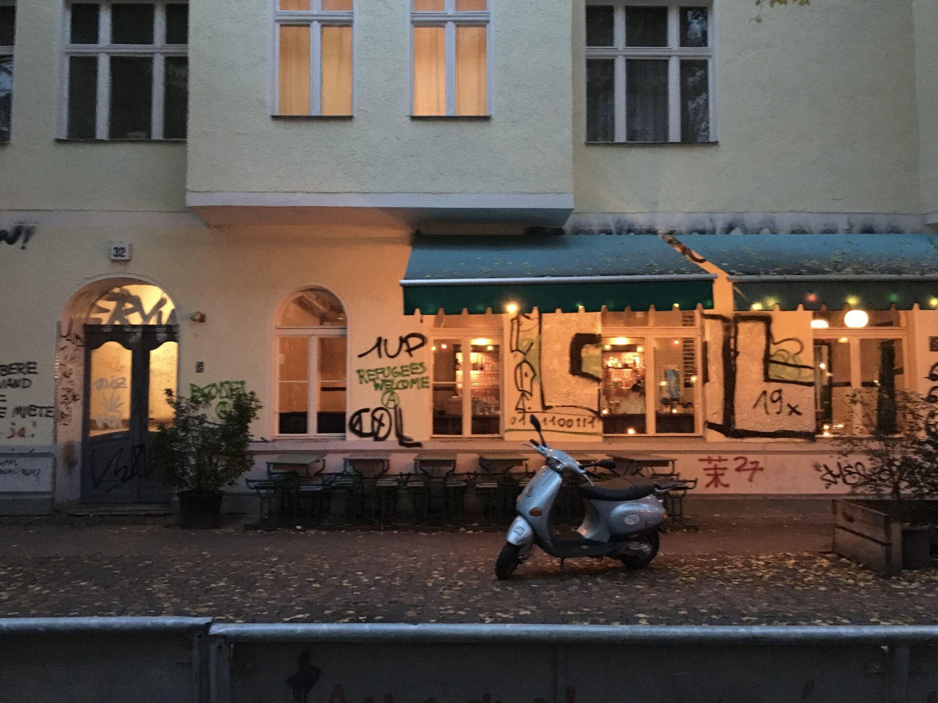 A moped is parked in front of a cafe in Berlin with the words "Refugees Welcome" written in grafiti