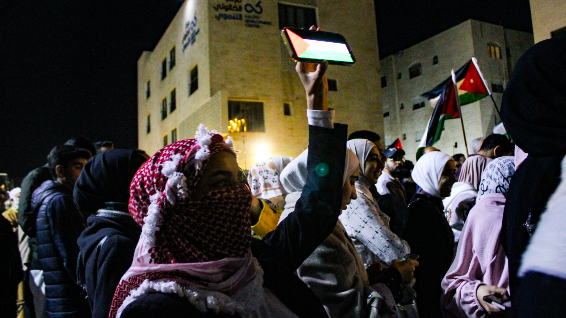 Women hold up their phones showing Palestinian flags at a demonstration outside the Israeli embassy on Saturday April 6, Jordanian flags wave in the background (Hanna Davis)