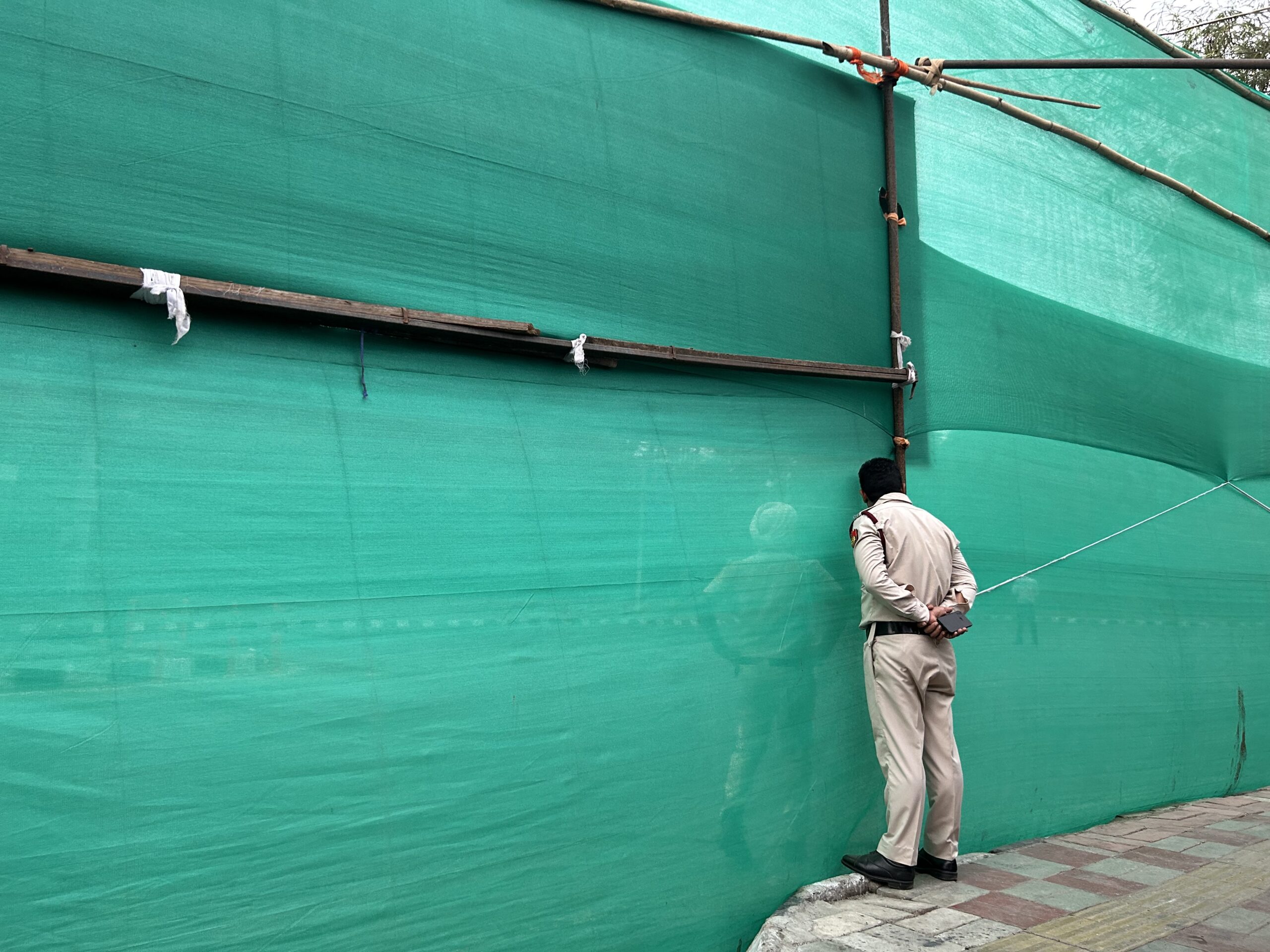 A Delhi Police official looks through the green curtain during the VIP movement