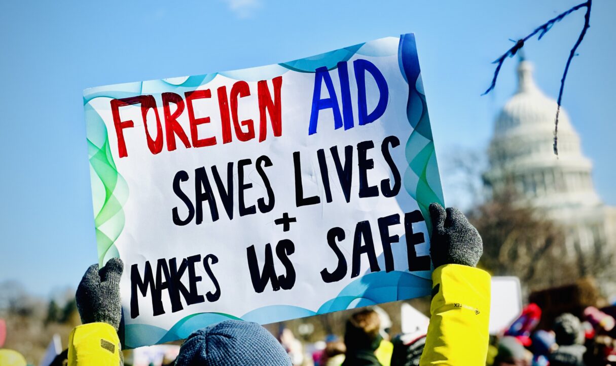 During a President's Day protest in February 2025, a demonstrator holds a placard in support of foreign aid (StephenLukeEdD/Wikimedia Commons)