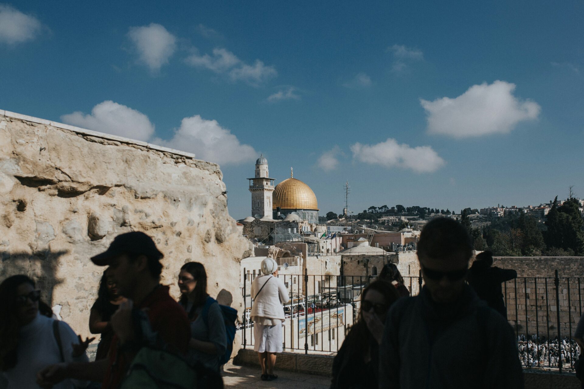 Silhouettes of tourists blur past a woman viewing holy sites in Jerusalem's historic old city (Cole Keister via Unsplash)