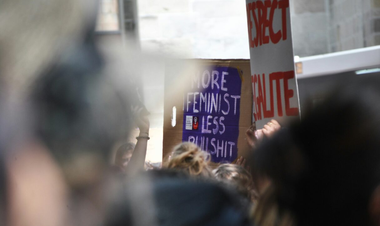 a protest with a sign that reads, "more feminist less bullshit"