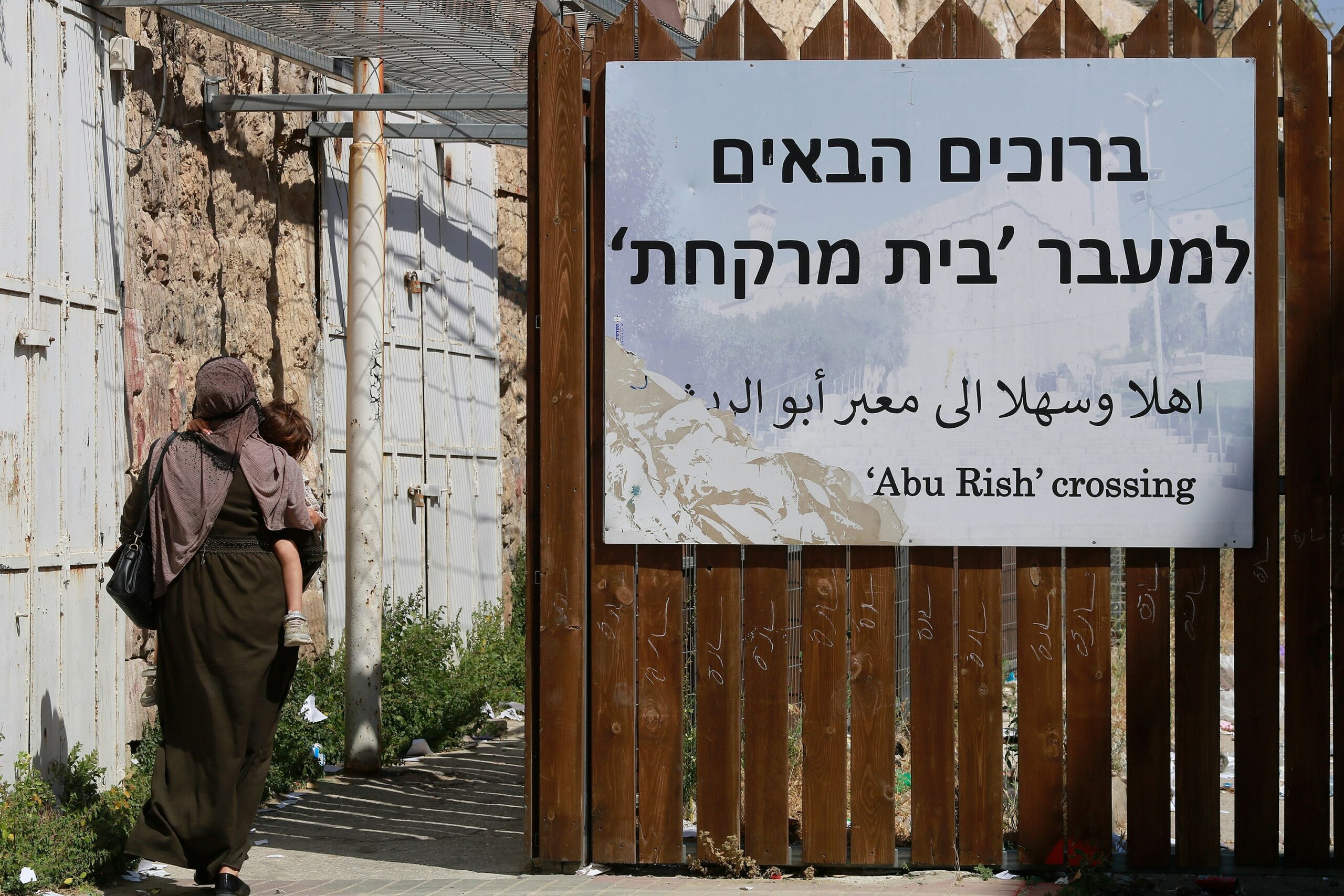 A woman and a child pass a crossing in the occupied West Bank city of Hebron in June 2023 (Diana Khwaelid/Unsplash)