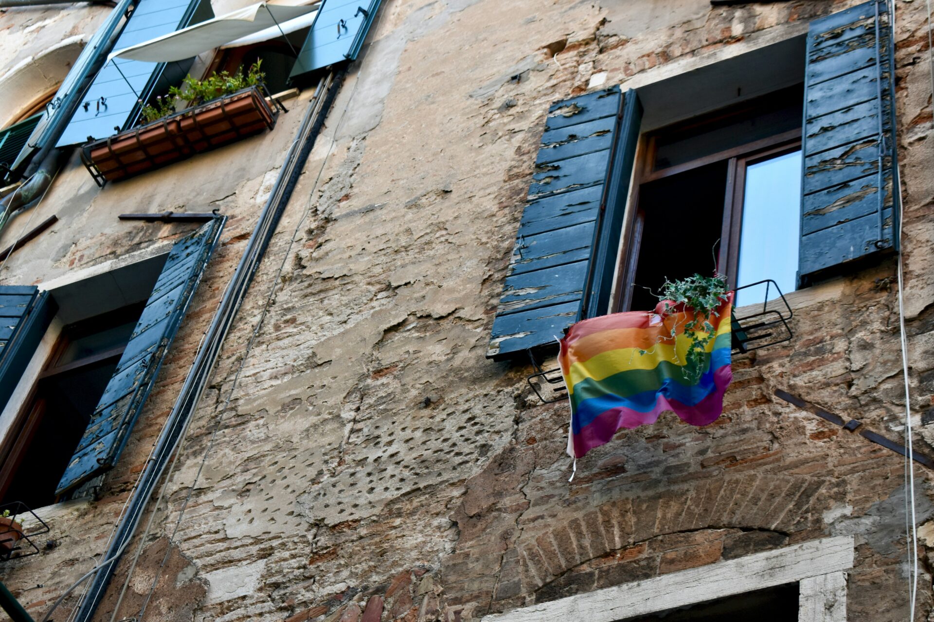 An LGBTQ flag hangs from a window in Venice, Italy, photographed in July 2021 (Faith Crabtree via Unsplash)