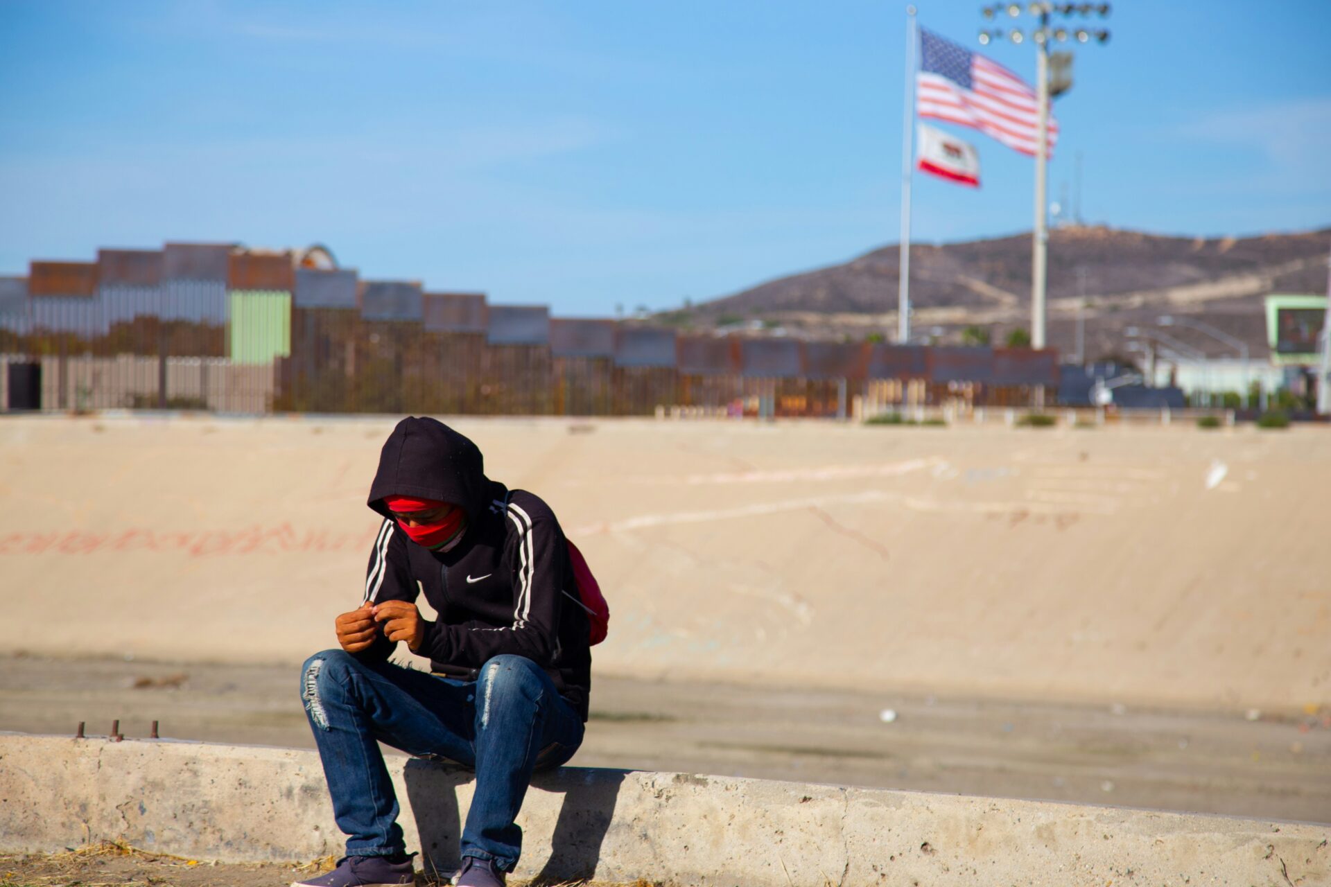 A young man sits waiting near the US-Mexico border in Tijuana, Mexico, published on Nov. 26, 2018 (Humberto Chávez/Unsplash)