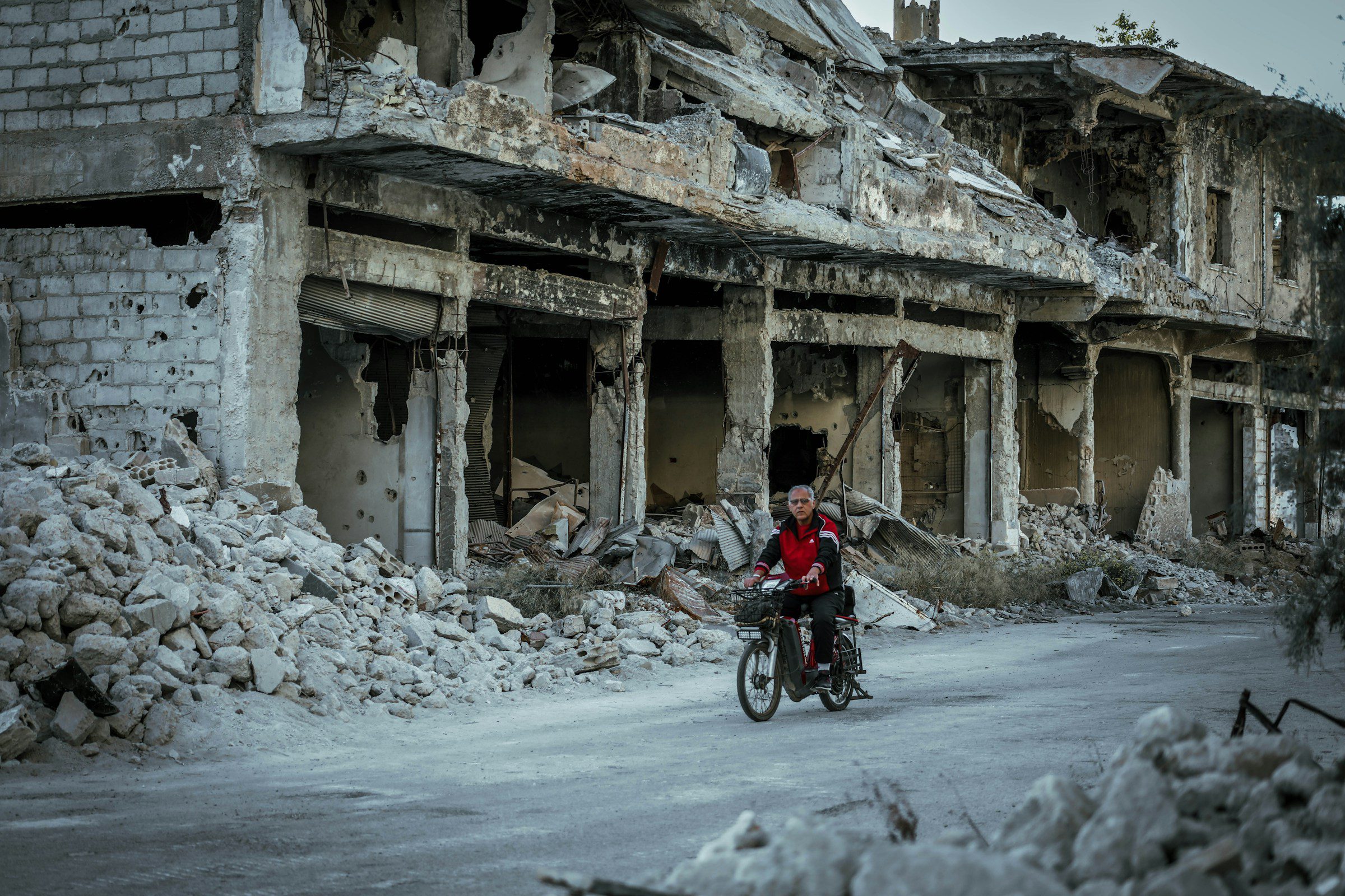 A man rides a motorcyle through rubble-lined streets in the Syrian city of Daraa, published on Jan. 27, 2022 (Mahmoud Sulaiman/Unsplash)