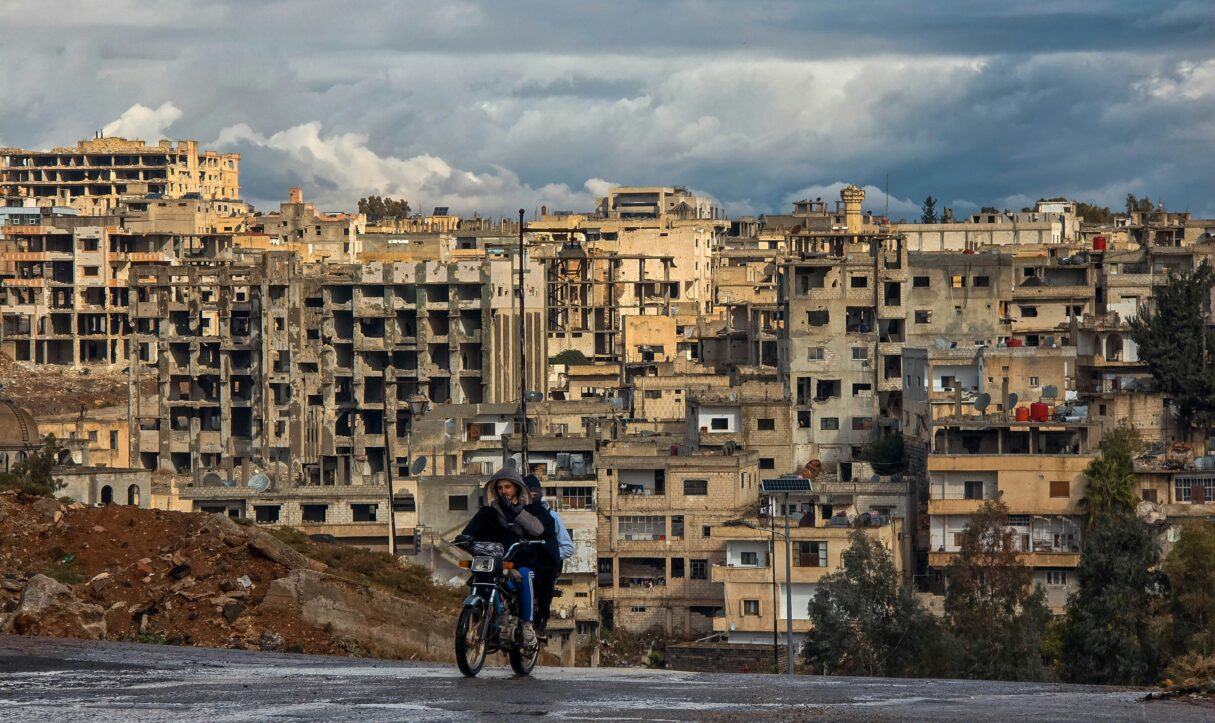 Two men ride a motorbike out of the Karak neighborhoood of Syria's Daraa city in January 2025 (Mahmoud Sulaiman/Unsplash)