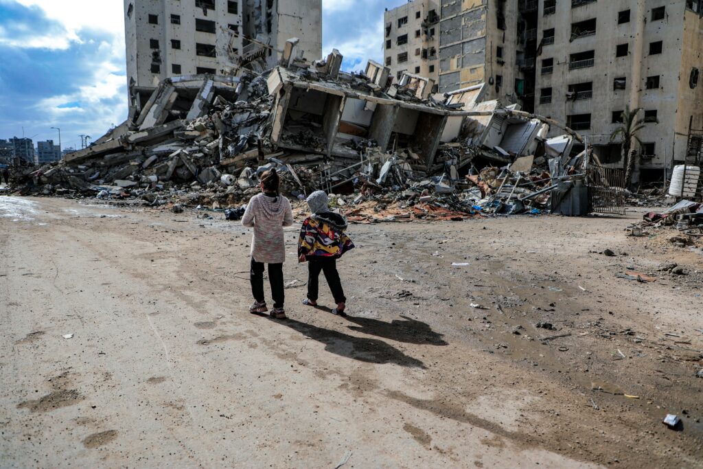 Children walk past rubble of a destroyed building in the war-ravaged Gaza Strip in July 2025 (Mohammed Ibrahim/Unsplash)
