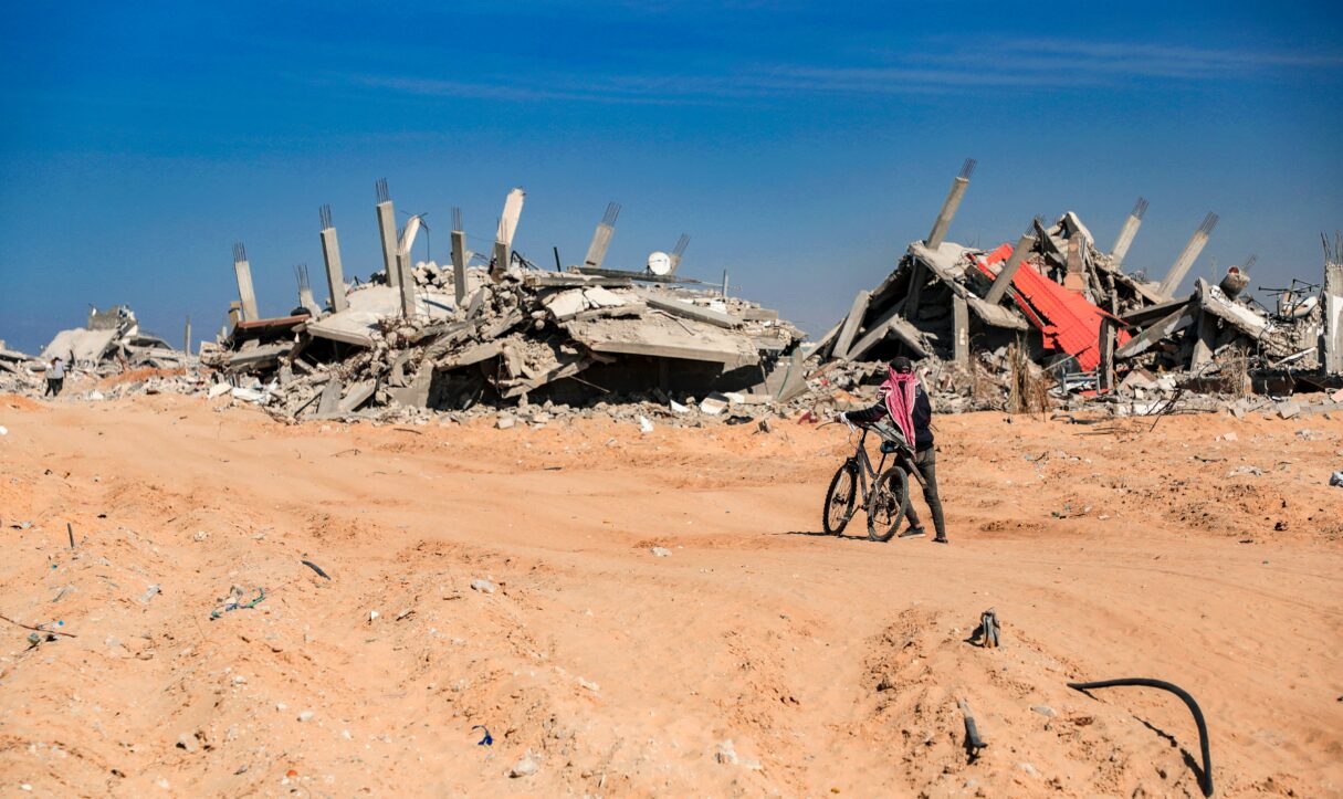 A young Palestinian pushes a bicycle through the sand and rubble caused by Israeli airstrikes in July 2025 (Mohammed Ibrahim/Unsplash)