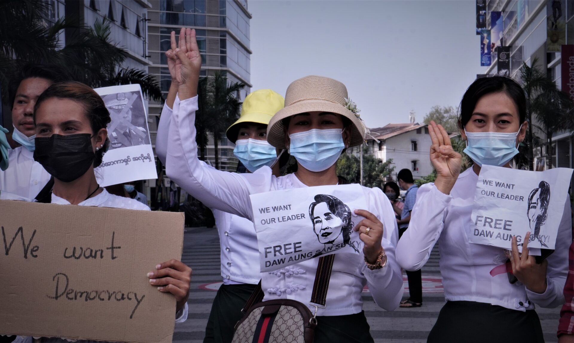 three people holding signs protesting for democracy for myanmar