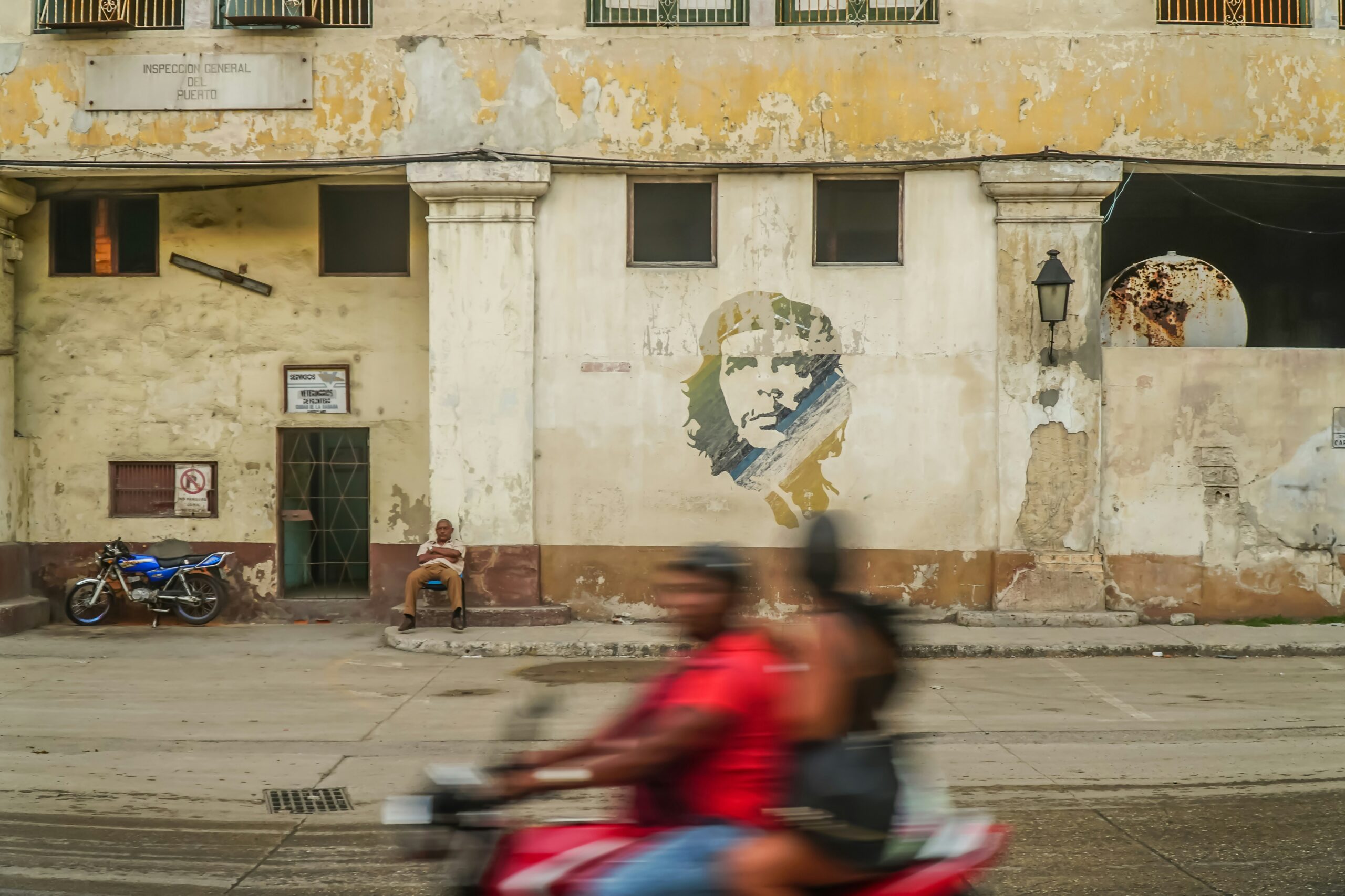 A man and a woman on a motorcycle drive past graffiti of Che Guevara in Havana, Cuba, in March 2020 (Tiago Claro/Unsplash)